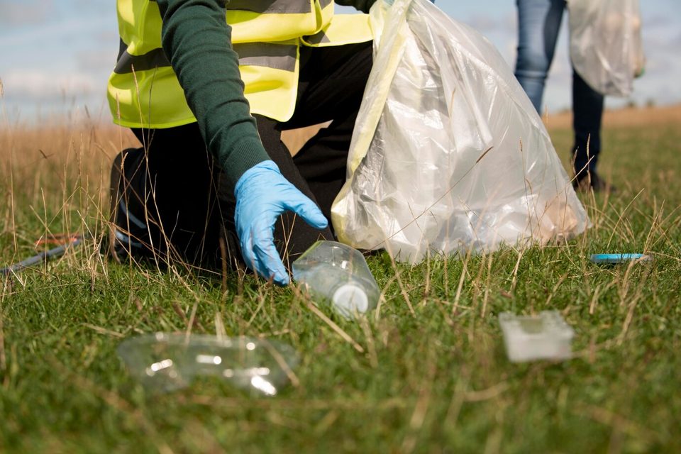 Volunteer in gloves picking up a plastic bottle from the grass
